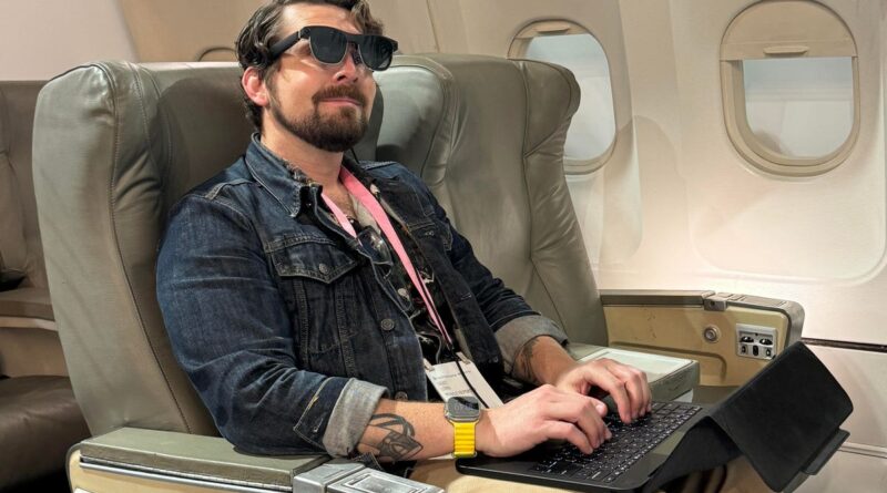 A man wears AR glasses connected to a laptop (without a display) while sitting in the seat of a mock-up airplane.